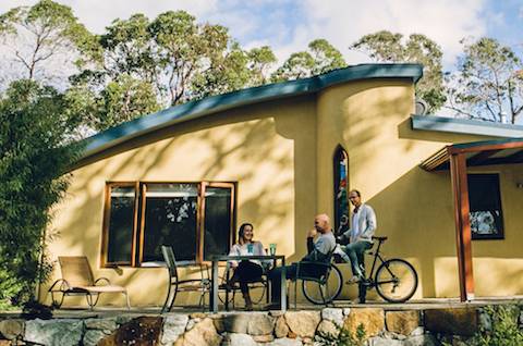 A couple sitting on a sunny patio talking to a man on a bike.