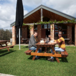 Two young men sitting outside a cellar door drinking wine.
